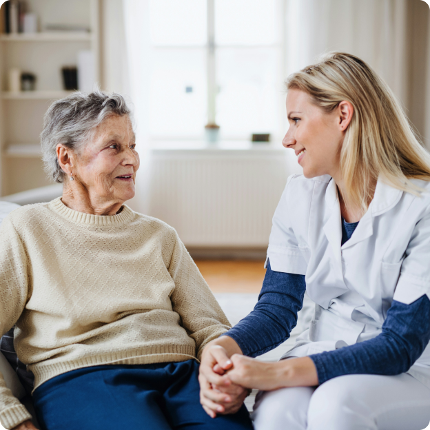 An eldely caucasian woman sitting and holding hands with a young caucasian nurse